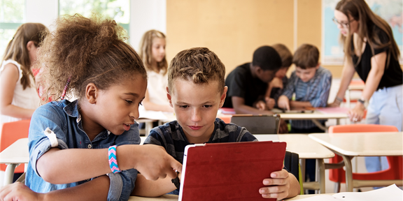 Zwei Kinder schauen sich im Klassenzimmer zusammen etwas auf ihrem Tablet an