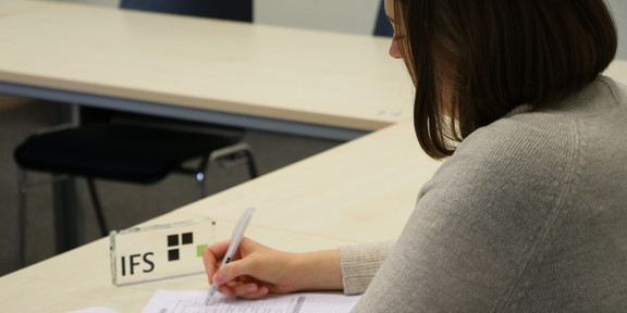 IFS Eine Person füllt einen Papierfragebogen neben einem IFS-Aufsteller aus