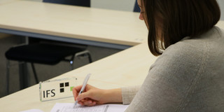 IFS Eine Person füllt einen Papierfragebogen neben einem IFS-Aufsteller aus