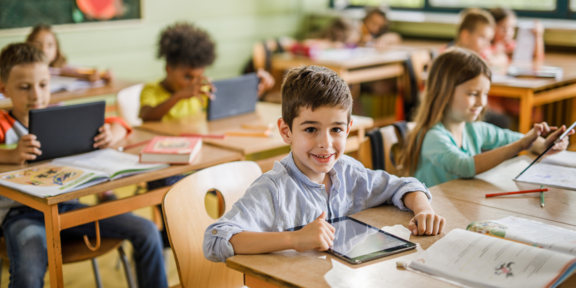 Schulklasse Grundschulkinder im Klassenraum, die mit Tablets und Schulheften arbeiten
