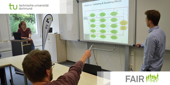 FAIR Graduierten Programm Logos der TU Dortmund und FAIR vor einer Seminarsituation mit Dozierenden und einem Teilnehmenden, der auf eine Präsentation deutet