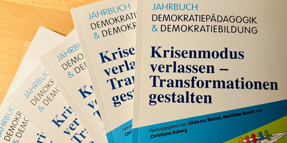 Mehrere Buchbänder des "Jahrbuch Demokratiepädagogik & Demokratiebildung" gefächert übereinanderliegend