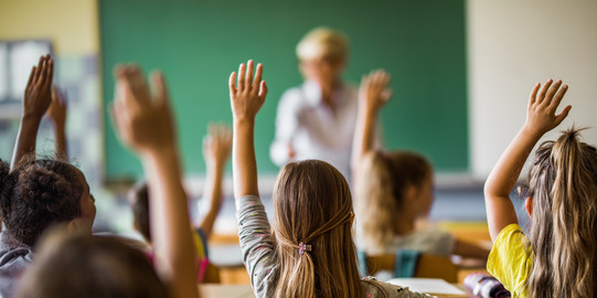 Schülerinnen und Schüler stimmen im Klassenraum mit Handzeichen ab