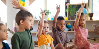 Mehrere Vorschulkinder sitzen im Klassenraum und melden sich