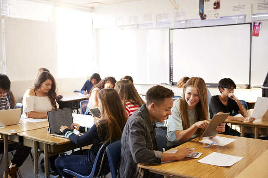 Foto eines Klassenzimmers, in dem Schülerinnen und Schüler an Tischen im Klassenzimmer sitzen und Laptops nutzen