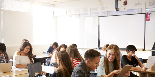 Foto eines Klassenzimmers, in dem Schülerinnen und Schüler an Tischen im Klassenzimmer sitzen und Laptops nutzen
