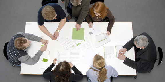 Studierende und Dozierende sitzen gemeinsam an einem Tisch und arbeiten.